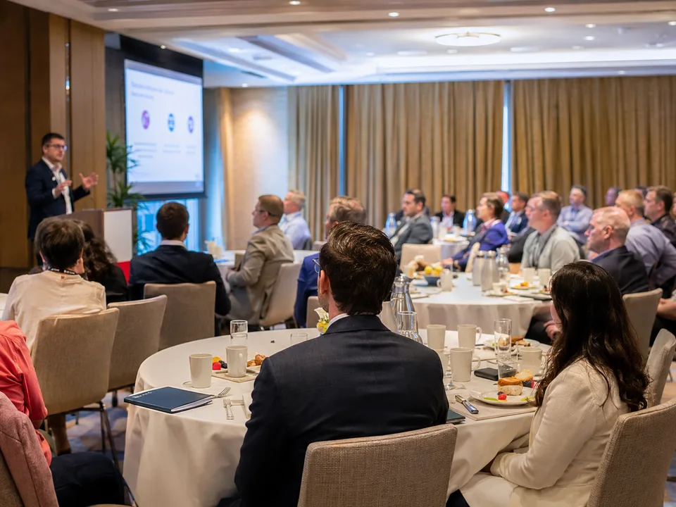 Full room of attendees at round tables listening to a morning presentation.