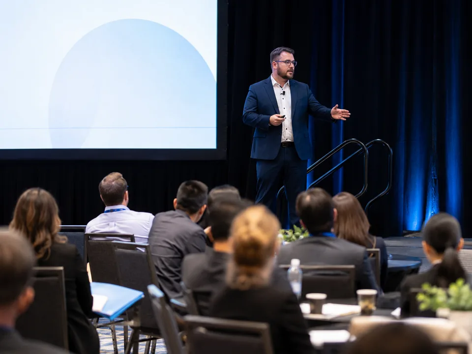 Keynote speaker gesturing to a conference audience from the stage.
