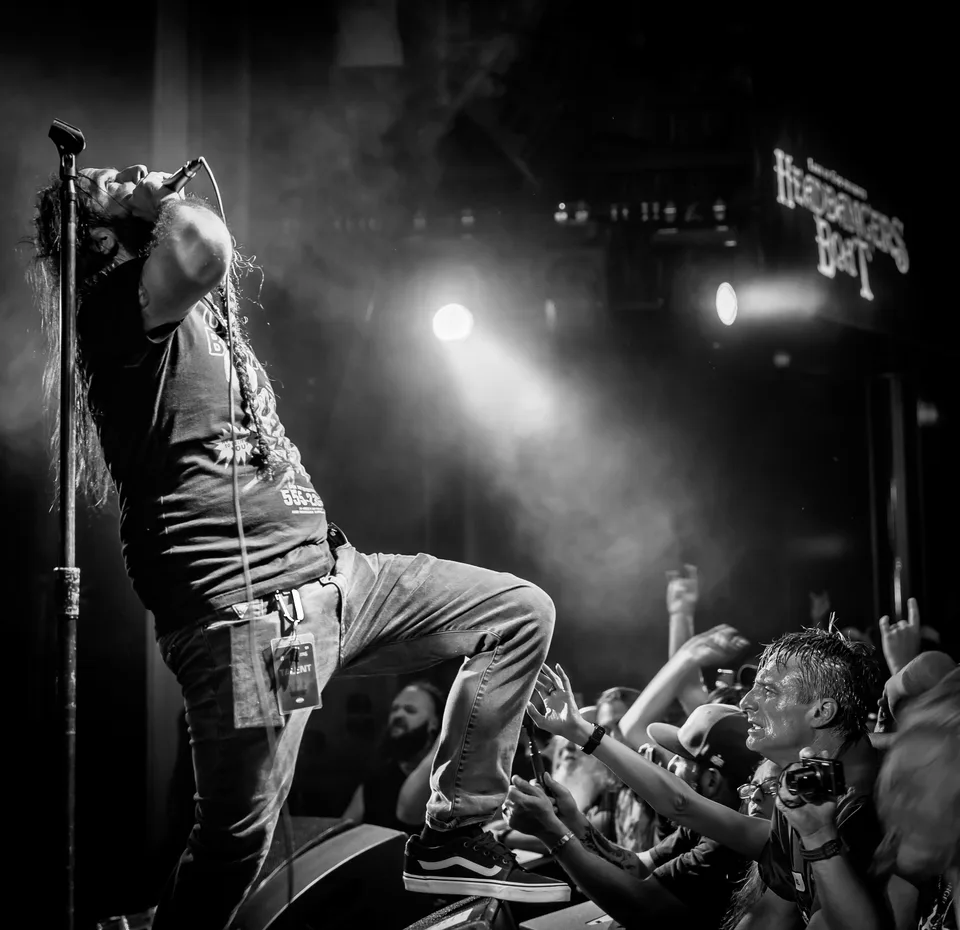 Wide black-and-white frame of a vocalist on stage above a sea of reaching hands.