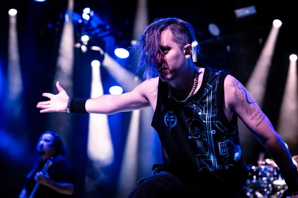 Frontman in blue stage light reaching out over the crowd mid-song.